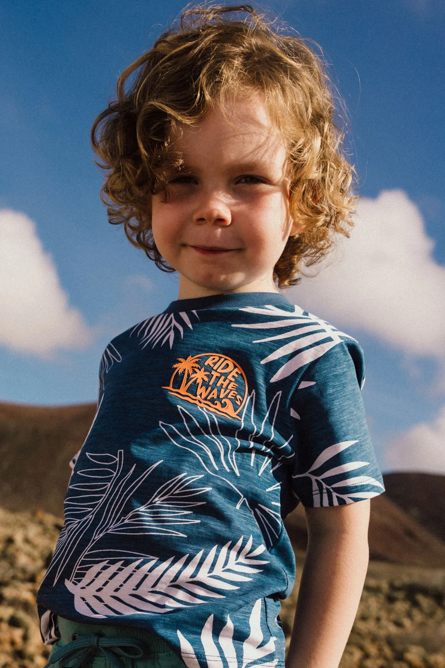 Maglietta in maglia per bambino di colore blu con design tropicale.